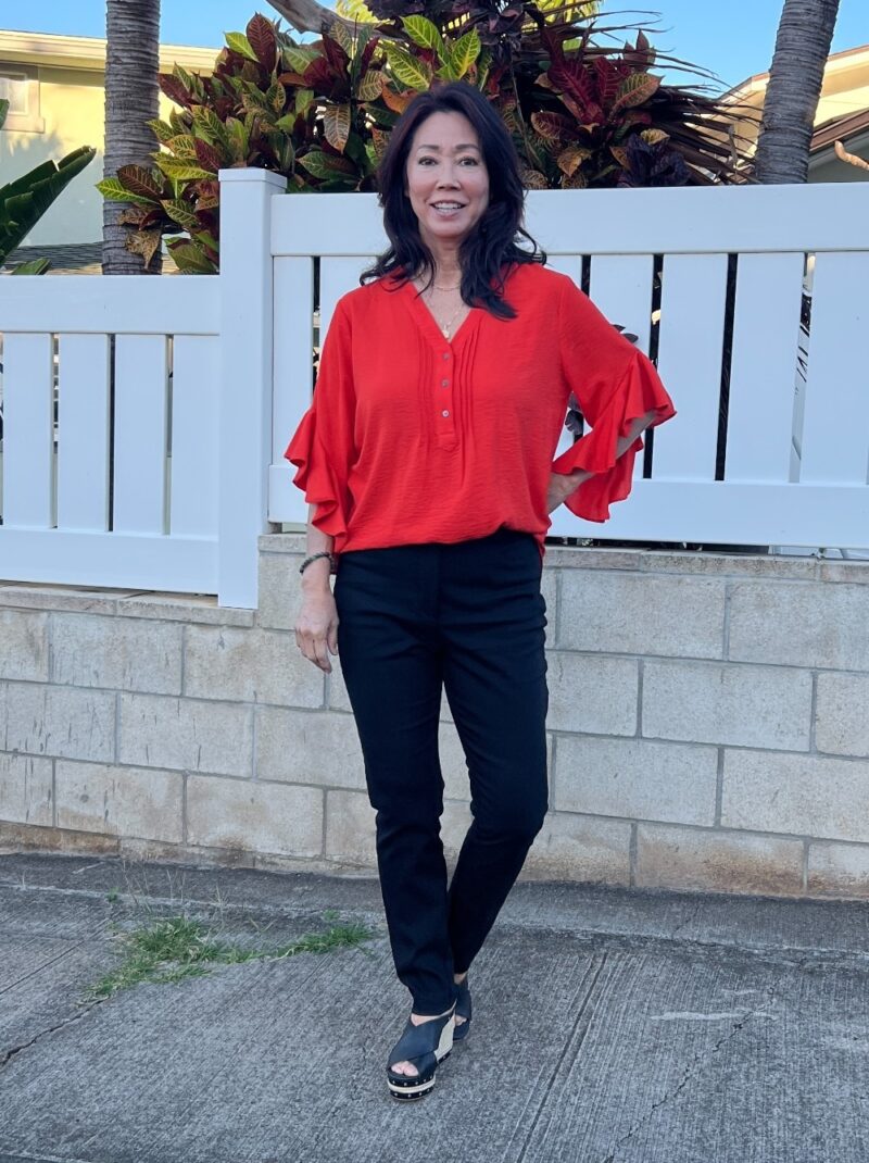 orange flutter sleeve blouse with black pants and black slip on espadrilles